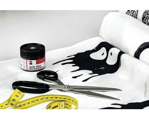 Textilfarbe, Schere und Massband auf einem Stoff mit Muster