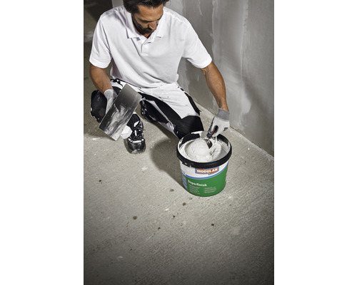 Un homme prépare du mastic dans un seau pour l''appliquer sur un mur.