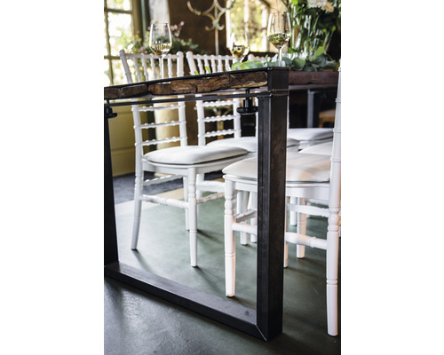 Nahaufnahme eines Esstisches mit Metallgestell und Holzplatte, umgeben von weißen Stühlen.