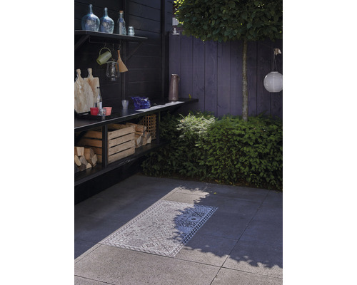 Aussenbereich mit Holzkohlegrill, Holzlager und dekorativem Teppich auf Steinplatten