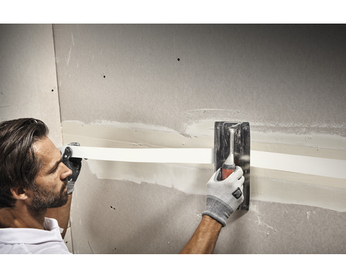 Ein Mann verspachtelt eine Gipskartonwand mit einem Spachtel und einem Armierungsstreifen.