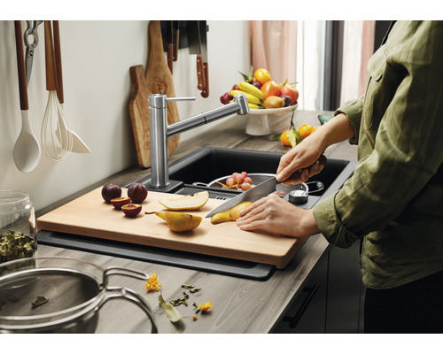 Küchenszene mit Spüle, Armatur, Schneidebrett und Person, die Obst schneidet