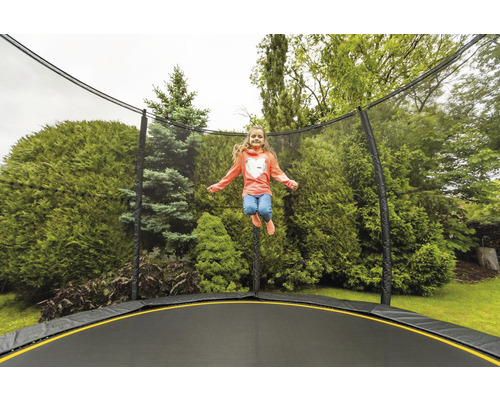 Fille sautant sur un trampoline de jardin avec filet de sécurité devant des arbres