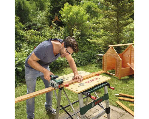 Mann sägt Holz mit einer Handkreissäge auf einer Bosch Werkbank im Garten.