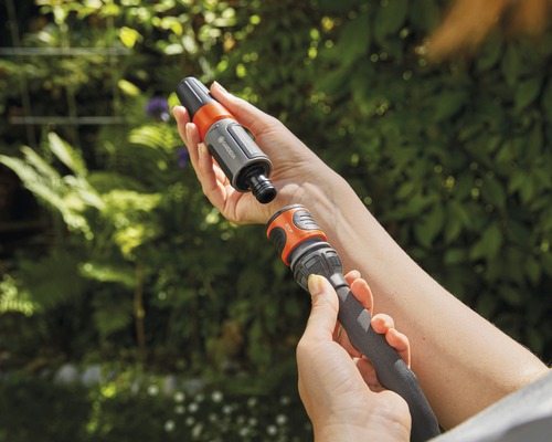 Person verbindet Gardena Schlauchstück mit Gartenschlauch vor Pflanzen
