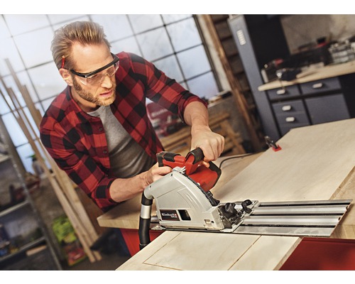 Un homme scie une planche de bois avec une scie plongeante dans un atelier.
