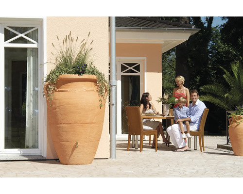 Gartenansicht mit großer Amphore als Regenspeicher bepflanzt neben Terrasse mit Familie