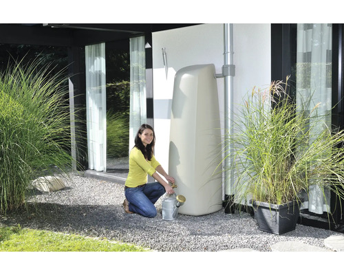 Une femme remplit un arrosoir à partir d''un réservoir d''eau vertical dans le jardin.
