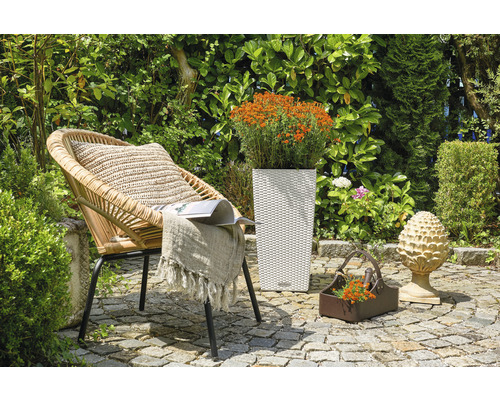 Gartenszene mit Korbsessel, Pflanzgefäß und Dekoration auf Steinboden