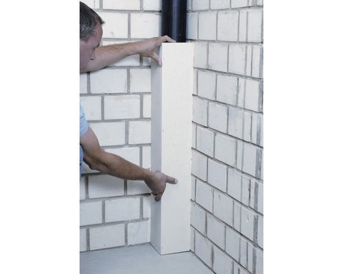 Un homme installe un profilé d''angle sur un mur en briques.