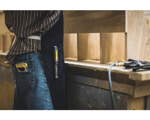 Handwerker mit Maßband, Arbeitsleuchte und Druckluftnagler bei der Arbeit mit Holz