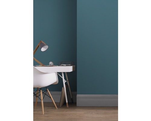 Ein Arbeitszimmer mit einer Arbeitsfläche, einem Stuhl und einer Lampe vor einer Wand.