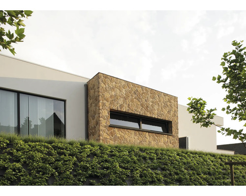 Außenansicht eines modernen Hauses mit Natursteinfassade und begrüntem Hang