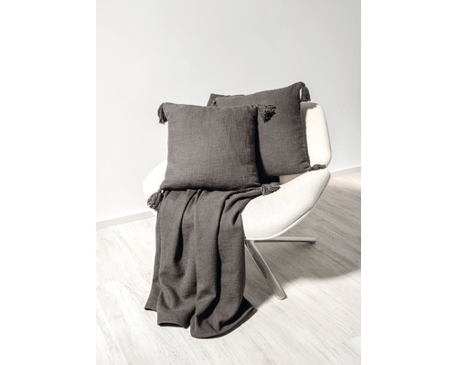 Sessel mit grauer Tagesdecke und zwei grauen Kissen mit Quasten