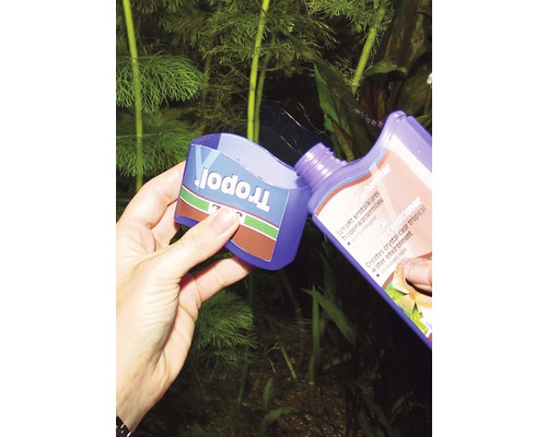 Eine Person giesst Tropopol Wasseraufbereiter in einen Messbecher vor einer Aquariumpflanze.