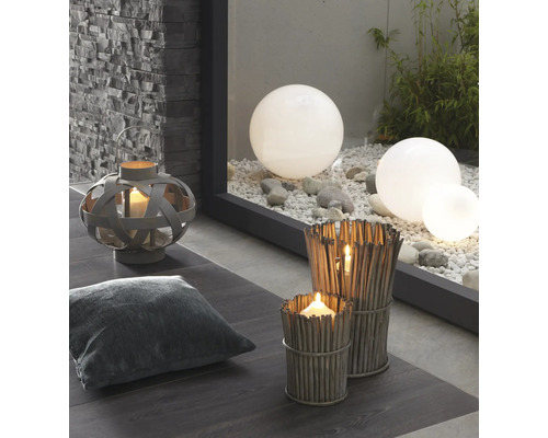 Dekorative Szene mit Laterne, Kissen, Windlichtern aus Zweigen und Gartenkugeln auf Kies