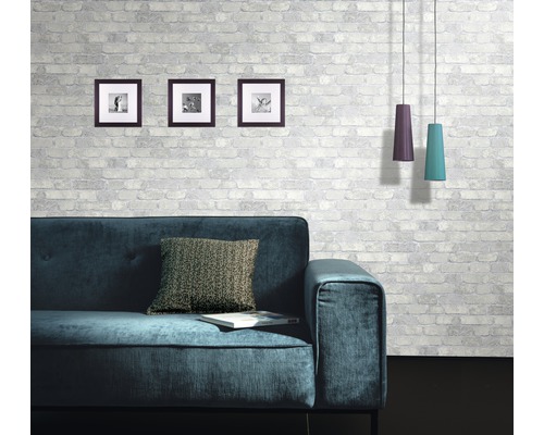 Wohnzimmer mit Sofa, Kissen, Bildern und Pendelleuchten vor einer gemusterten Ziegelwand