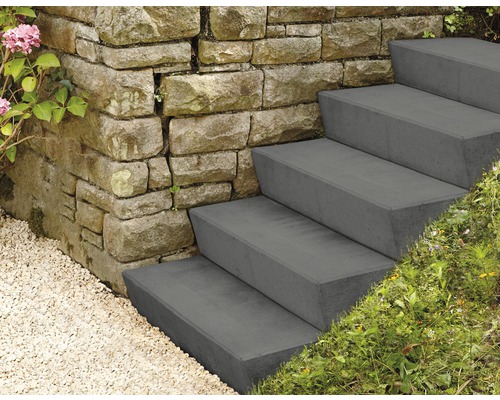 Außentreppe aus Beton neben einer Steinmauer mit Kies und Pflanzen.