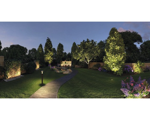 Beleuchteter Garten mit Rasen, Bäumen, Blumen und Steinweg bei Dämmerung