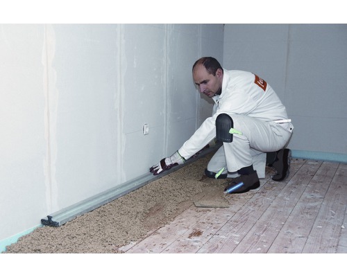 Artisan nivelant le remblai sec avec une règle sur un plancher en bois.