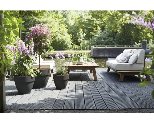 Terrasse mit Pflanzgefäßen, Holztisch und Sofa am Wasser