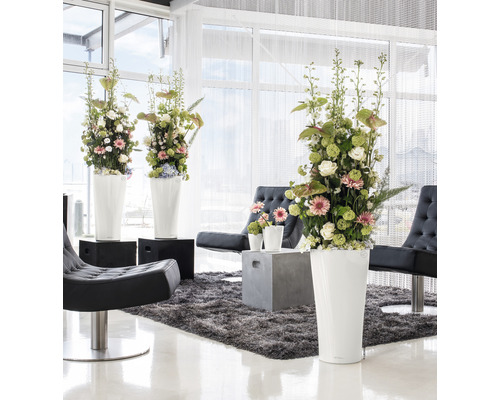 Helle Inneneinrichtung mit Blumenarrangements in hohen Pflanzgefäßen, Sesseln und Teppich