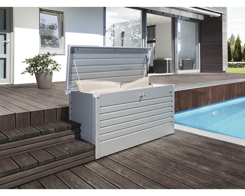 Geöffnete Aufbewahrungsbox aus Metall mit Kissen auf einer Holzterrasse neben einem Pool