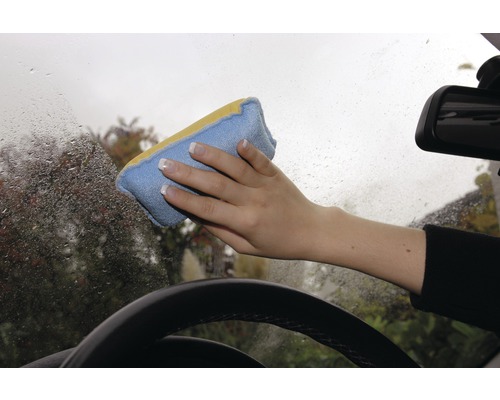 Une main essuie un pare-brise mouillé avec une éponge de nettoyage