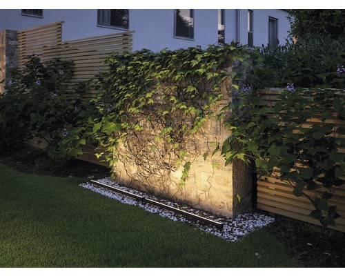 Beleuchtete Gartenmauer mit Bewuchs und Rasenfläche.