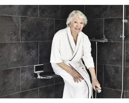 Femme assise sur un siège de douche dans une douche à l''italienne avec des carreaux gris.