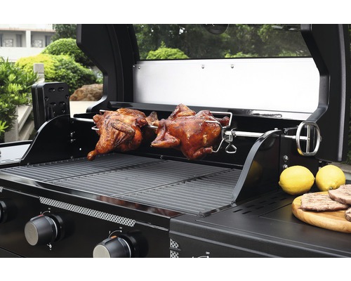 Gril à gaz avec deux poulets rôtis sur une broche et des citrons sur une planche en bois