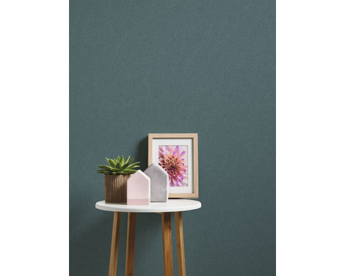 Dekorative Szene mit Topfpflanze, Hausfiguren und gerahmtem Bild auf einem runden Tisch vor einer gemusterten Wand