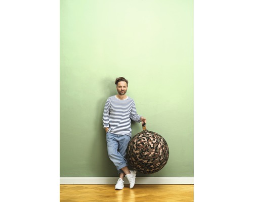 Un homme appuyé contre un mur tient un pouf rond à motif camouflage