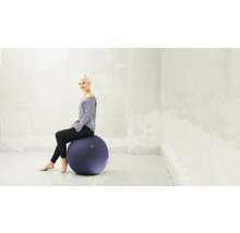 Femme assise sur un ballon de gymnastique bleu dans une pièce lumineuse.
