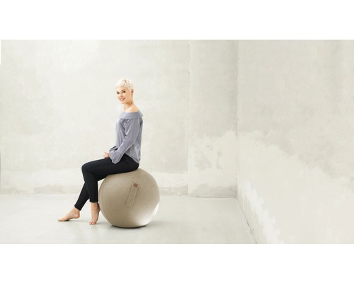 Femme assise sur un ballon de gymnastique dans une pièce lumineuse.