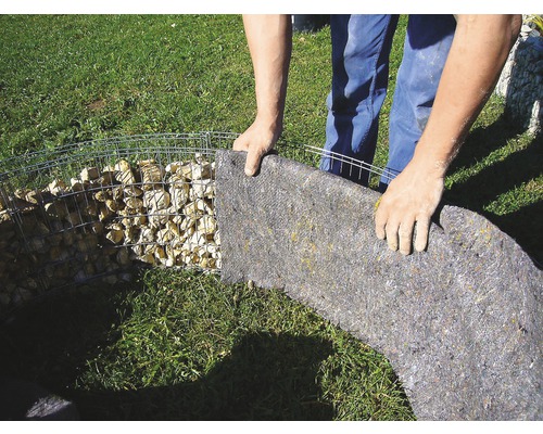 Person befestigt Trennvlies an einer Gabione im Garten.