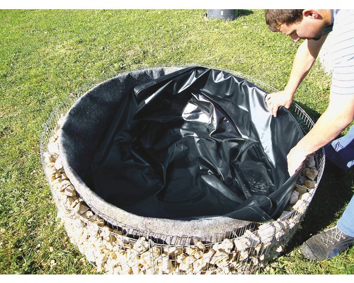 Ein Mann verlegt eine Teichfolie in einen runden, mit Steinen gefüllten Gabionenkorb