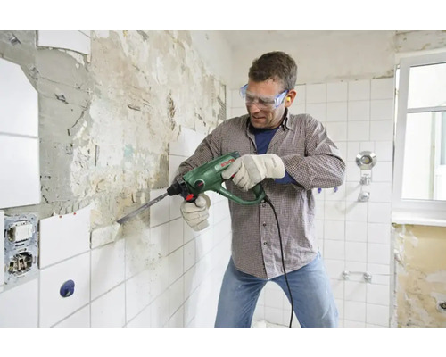 Un homme utilise un perforateur pour enlever des carreaux d''un mur de salle de bain.