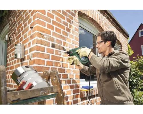 Un homme perce un trou dans un mur de briques avec une perceuse à percussion.