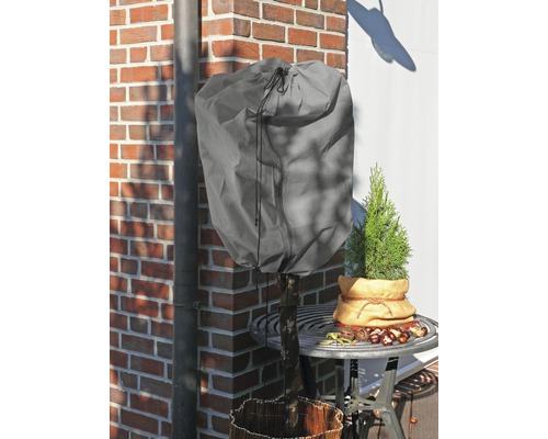 Plante avec housse de protection hivernale sur une table de jardin devant un mur de briques