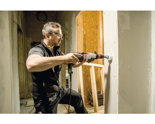 Un homme perce un trou dans un mur avec une perceuse sur un chantier.