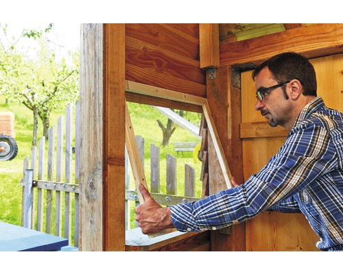 Mann baut Holzfenster in einem Gartenhaus ein