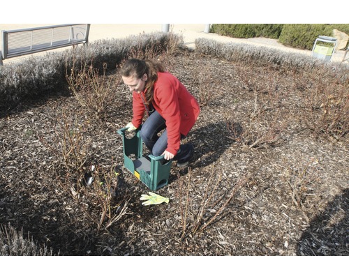 Une femme utilise un tabouret de jardin pour jardiner dans un parterre.