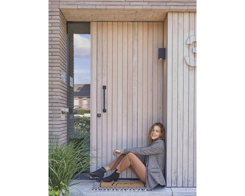 Frau sitzt vor einer Haustür mit Holzverkleidung und Hausnummer