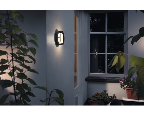 Beleuchtete Wandleuchte neben einem Fenster an einer Hauswand