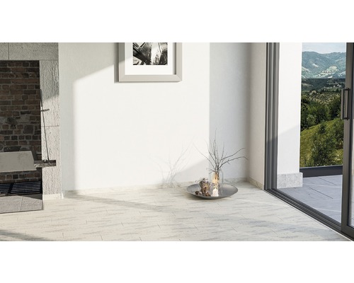 Pièce lumineuse avec carrelage au sol, tableau au mur et porte de terrasse donnant sur la verdure