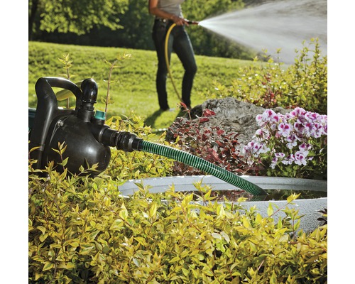 Garten mit Gartenpumpe, Schlauch und einer Person, die mit einem Gartenschlauch gießt