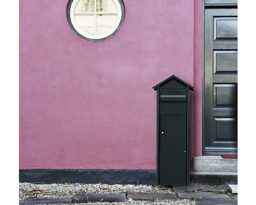 Boîte aux lettres autoportante devant un mur de maison avec porte et fenêtre