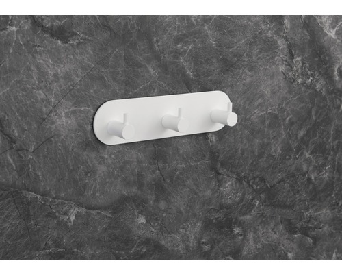 Porte-manteau mural blanc avec trois crochets sur un mur en marbre gris.