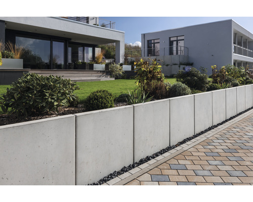 Jardin avec mur de soutènement en béton et chemin pavé devant des maisons modernes